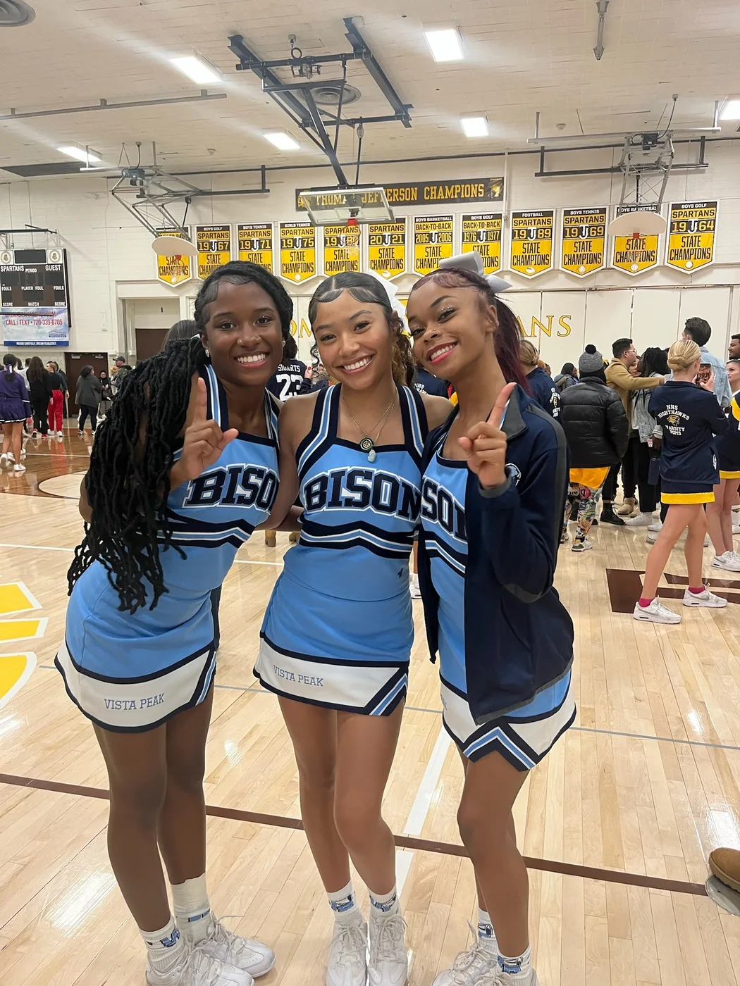 Syrai Smith with two cheer teammates in light blue uniforms, posing together in a gym.