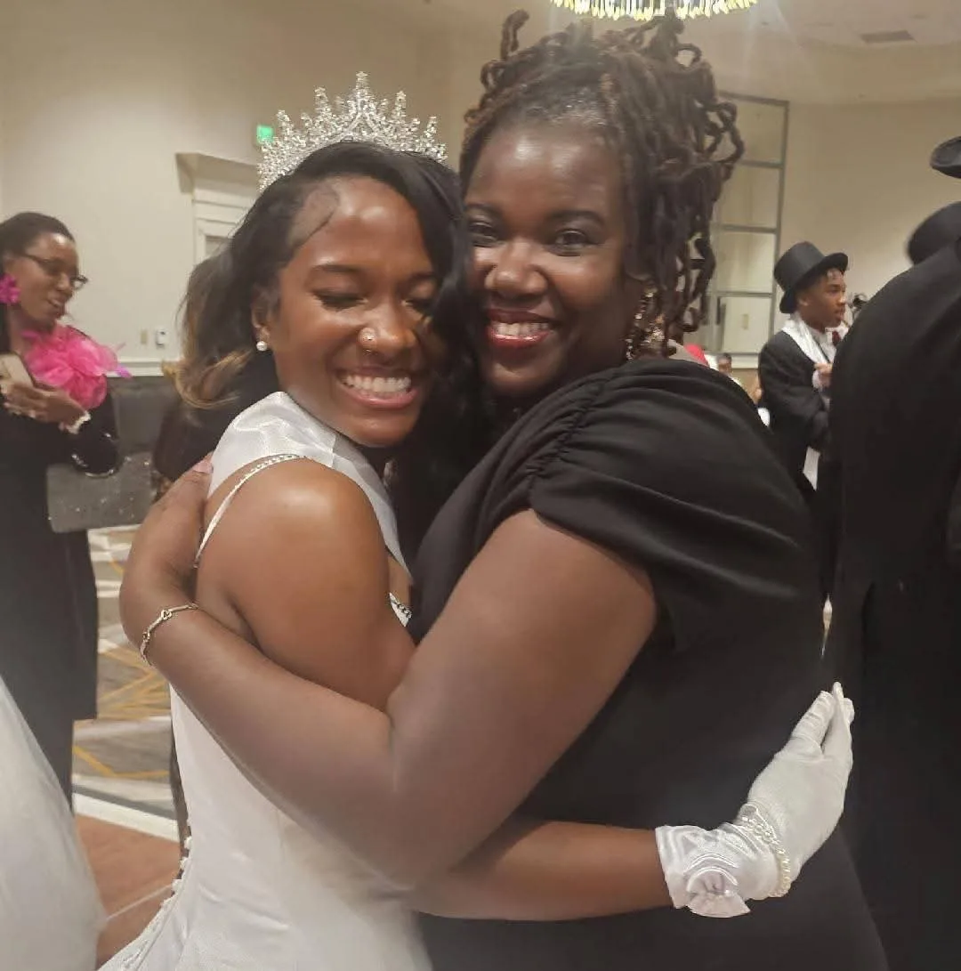 Syrai Smith in a white gown and tiara, eyes closed and smiling wide as she hugs a loved one.