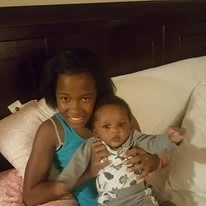A childhood photo of a young girl smiling and holding a baby.